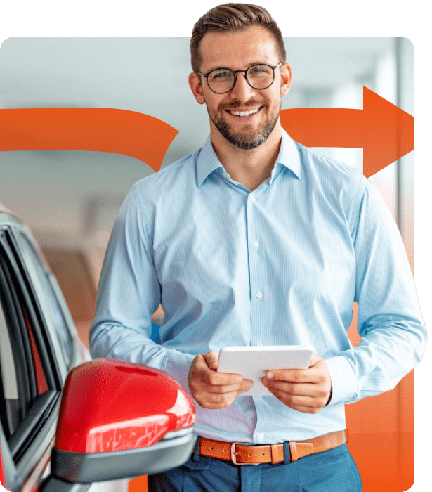 Man in blue dress shirt standing next to red car holding a tablet and smiling